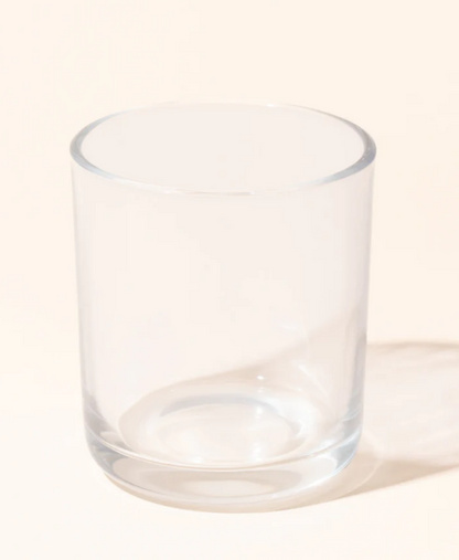 An empty clear glass tumbler casting a soft shadow on a beige background.