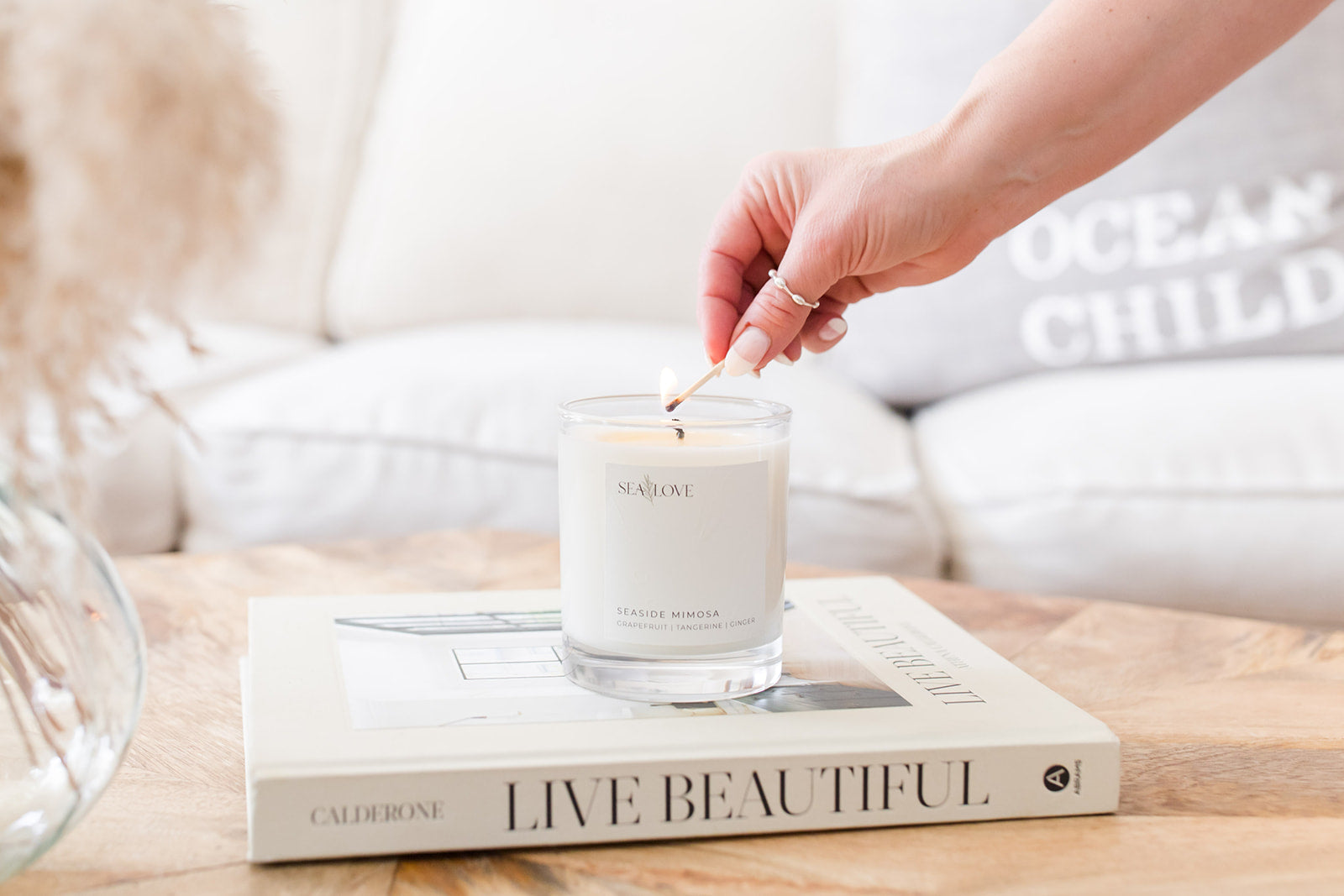A person lighting a scented candle placed on top of an aesthetic coffee table book, creating a serene and cozy atmosphere.