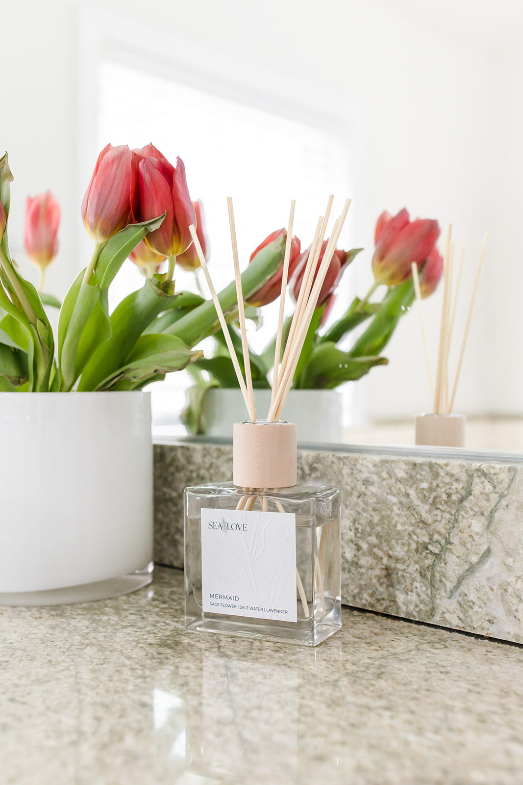 Elegant home fragrance diffuser with reed sticks placed on a marble countertop beside a bouquet of tulips, creating a fresh and inviting atmosphere.